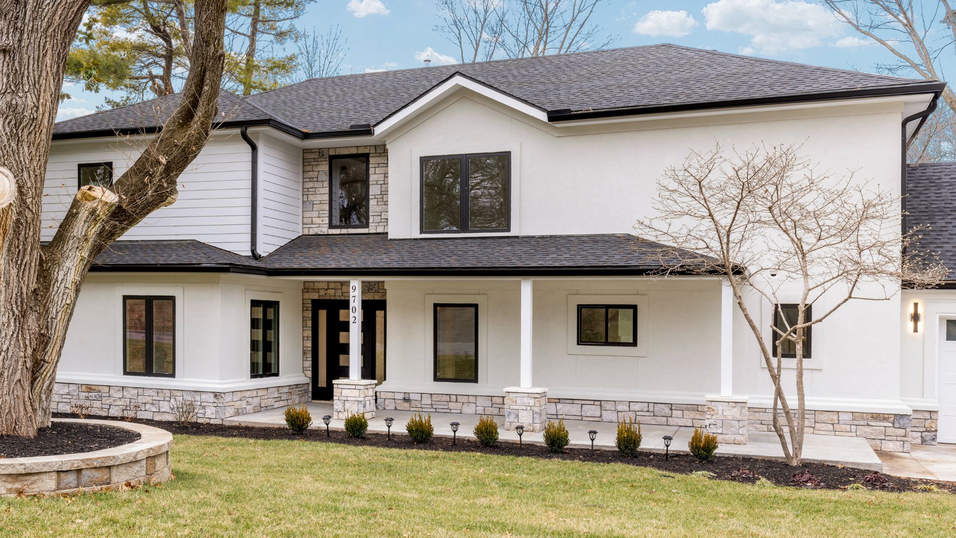 Front of remodeled home with white paint, stone and black roof.