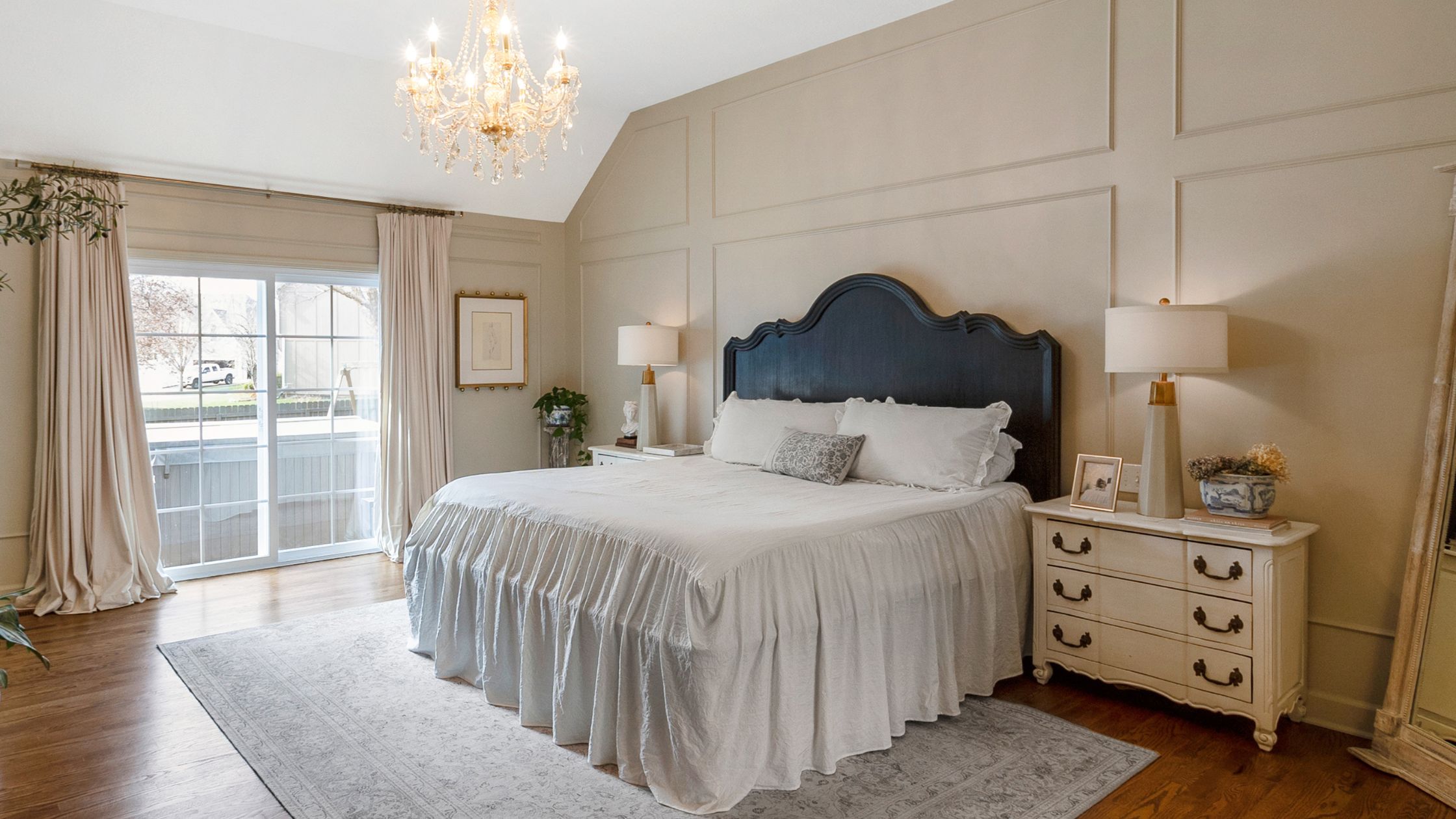 Neutral-painted bedroom with vintage-inspired decor including a chandelier, bed, two night stands and lamps.