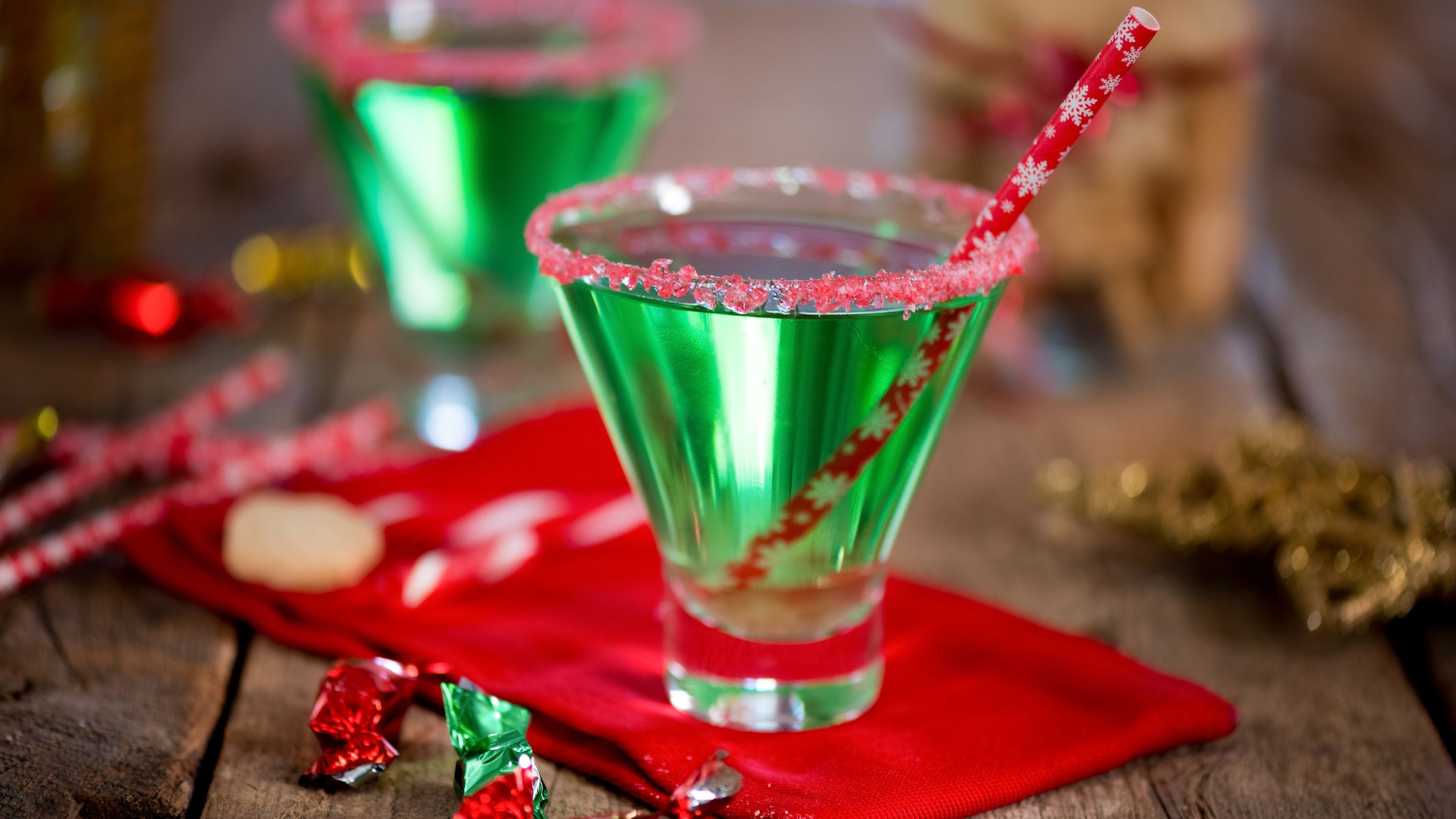 Green festive-looking drinks with red crystals around top and festive straw on red napkin.